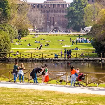 Milanese and tourists enjoy the Parco Sempione (Simplon park) overlooked by the towers of the Castello Sforzesco (Sforza Castle), on a sunny spring day.