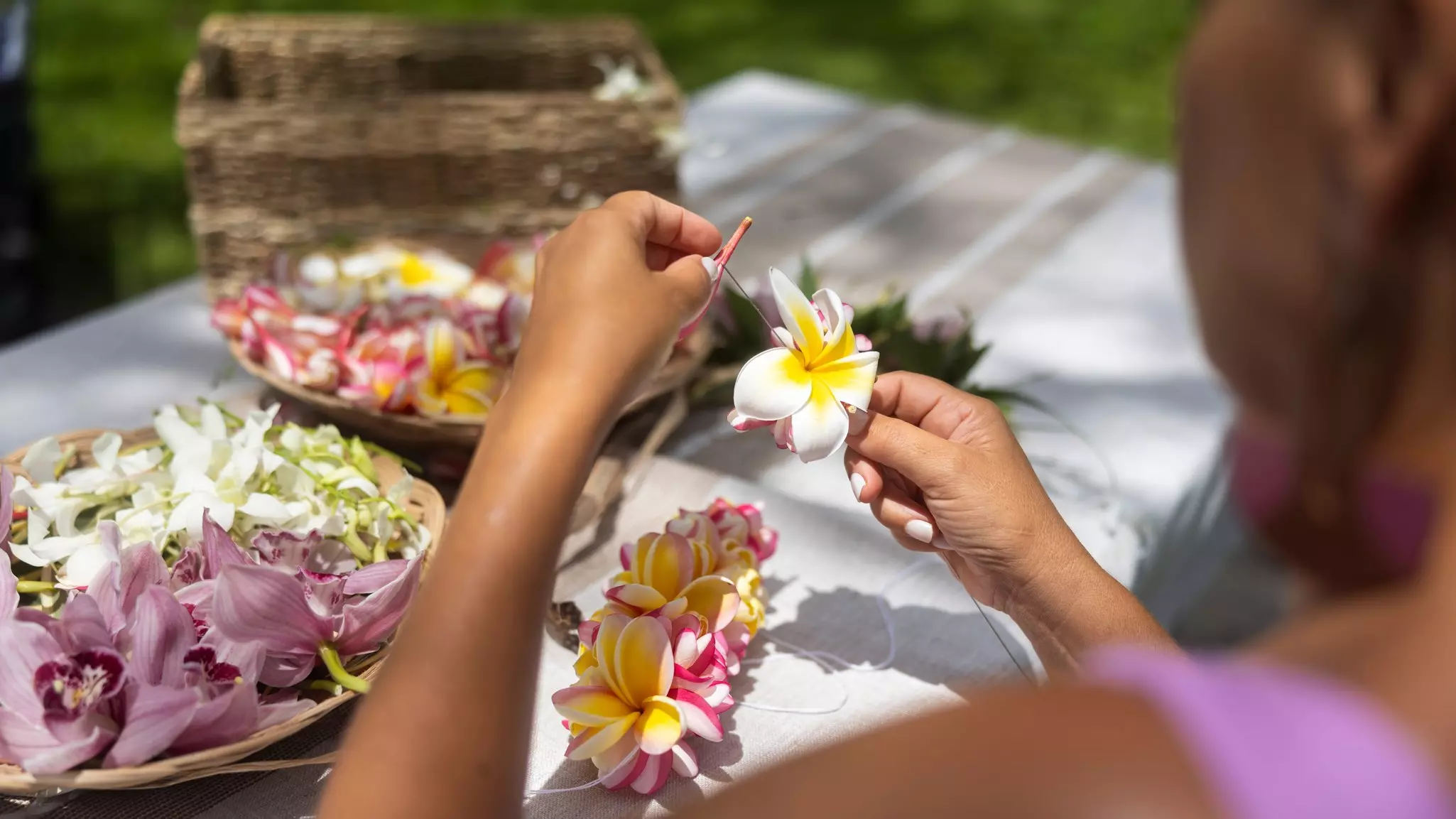 A person stitches together a lei, a flower garland, using yellow, pink and white flowers