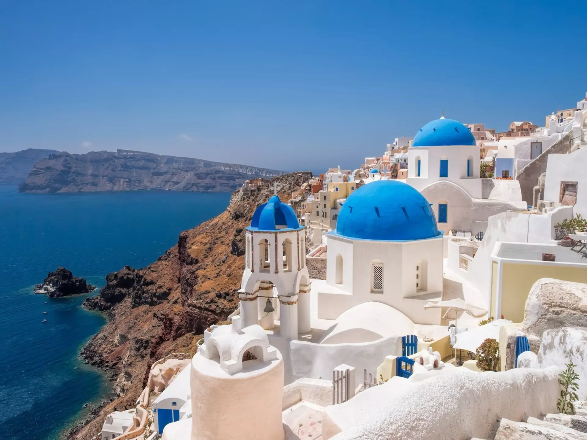 White buildings with blue accents on a hillside above the blue sea.