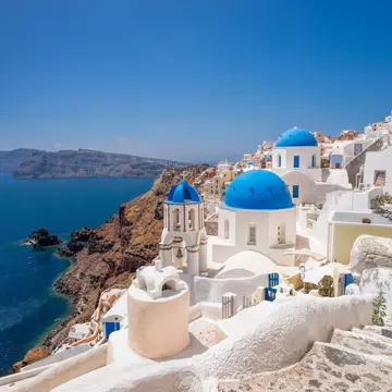 White buildings with blue accents on a hillside above the blue sea.