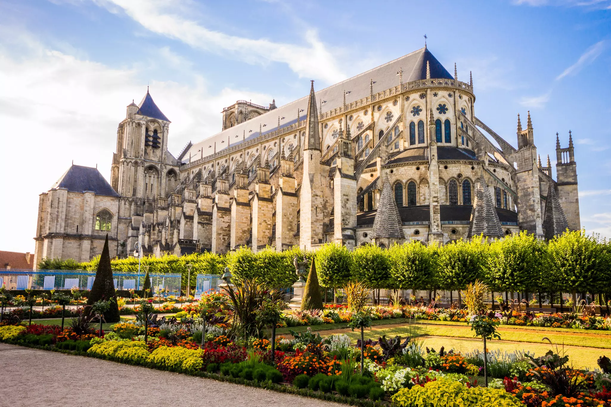 A large Gothic cathedral surrounded by a neat garden in bloom, in Bourges, France.