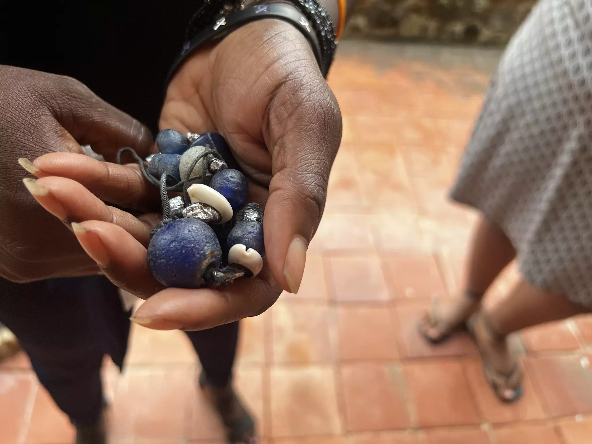 A hand holds a necklace with large round blue beads and smaller white shells.