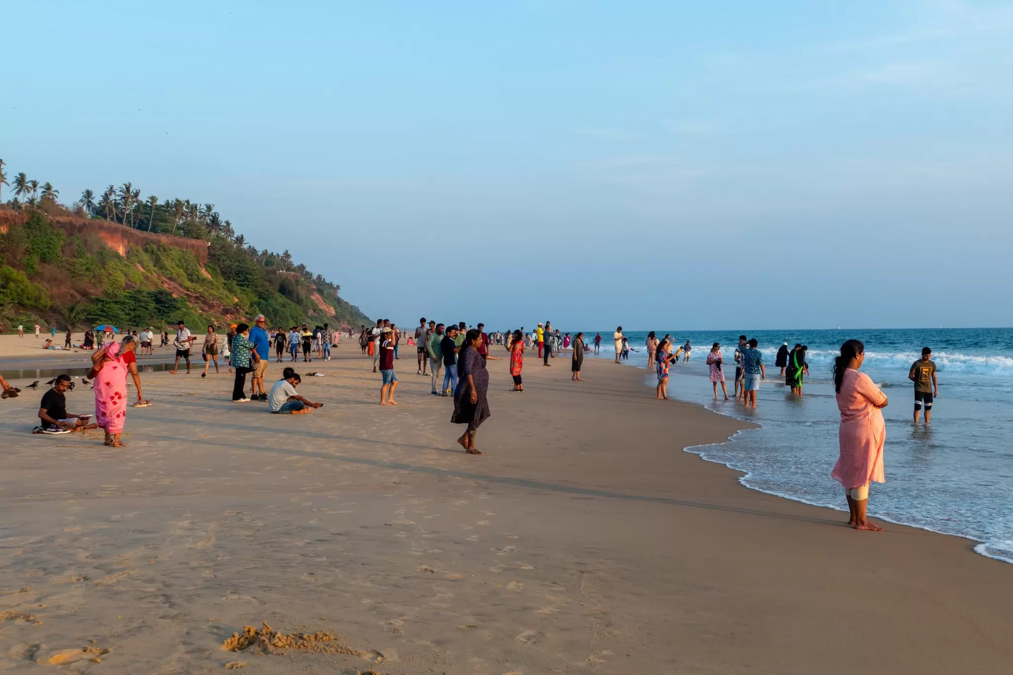 People stand on a sandy beach during sunset.