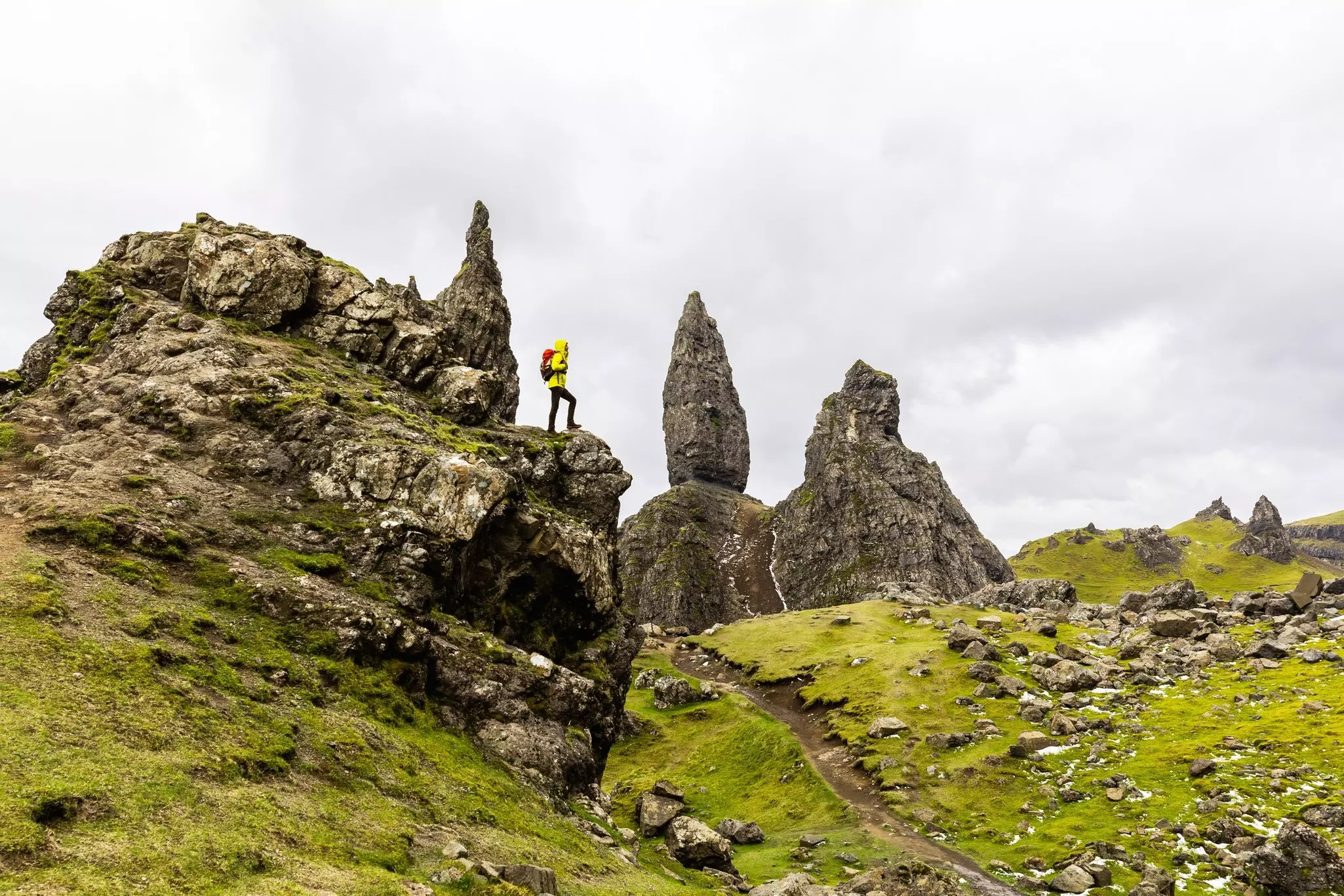 Man hiking in Scotland, Isle of Skye at the Old Man of Storr - Hiker climbing on rocks with the famous rock of the Isle of Skye on a cloudy  day
