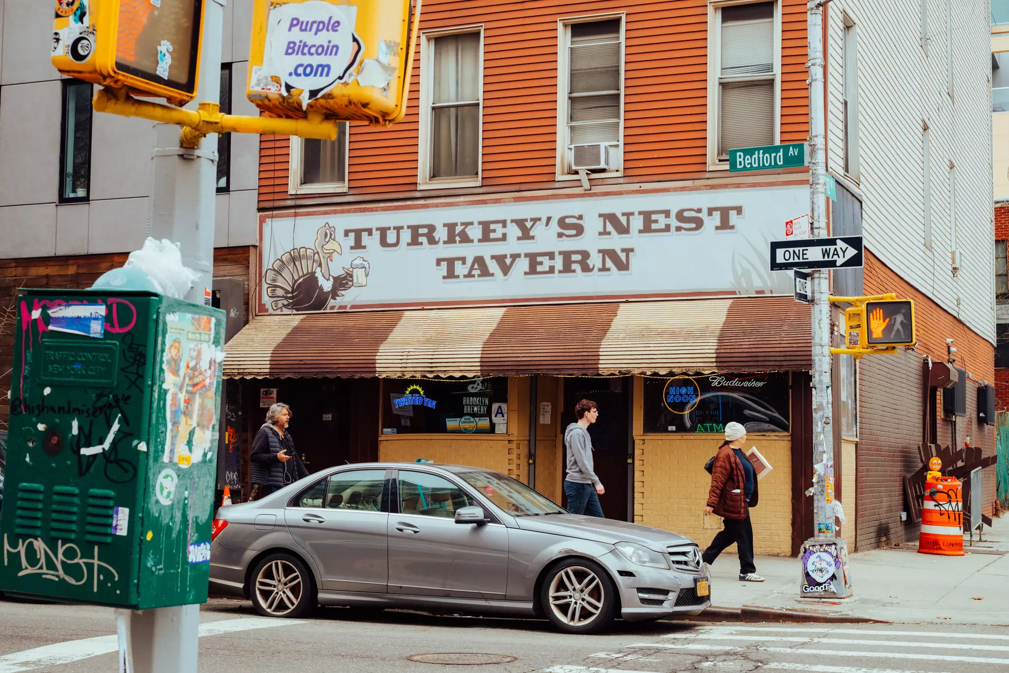 The facade of a bar in New York City a grey car parked outfront. The sign says Turkey's Nest Tavern and there is a picture of a turkey with a pint of beer.