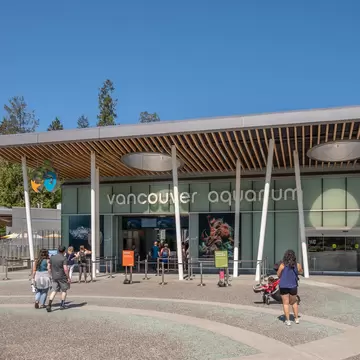 A low modern building with a slatted timber canopy signed Vancouver Aquarium, visitors crossing the paved forecourt towards it.