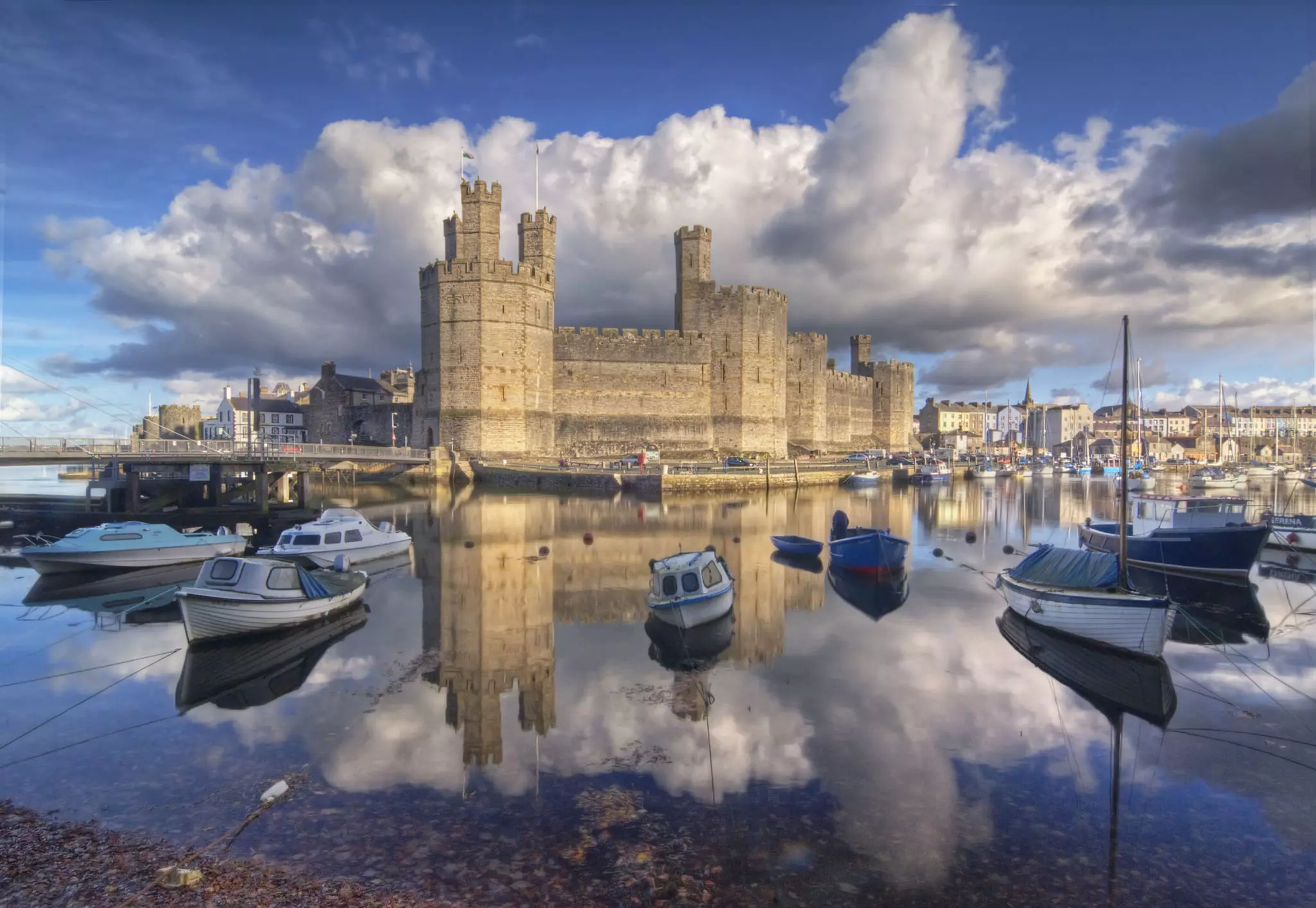 Caernarfon Castle reflected in the water, surrounded by boats, in Wales.
