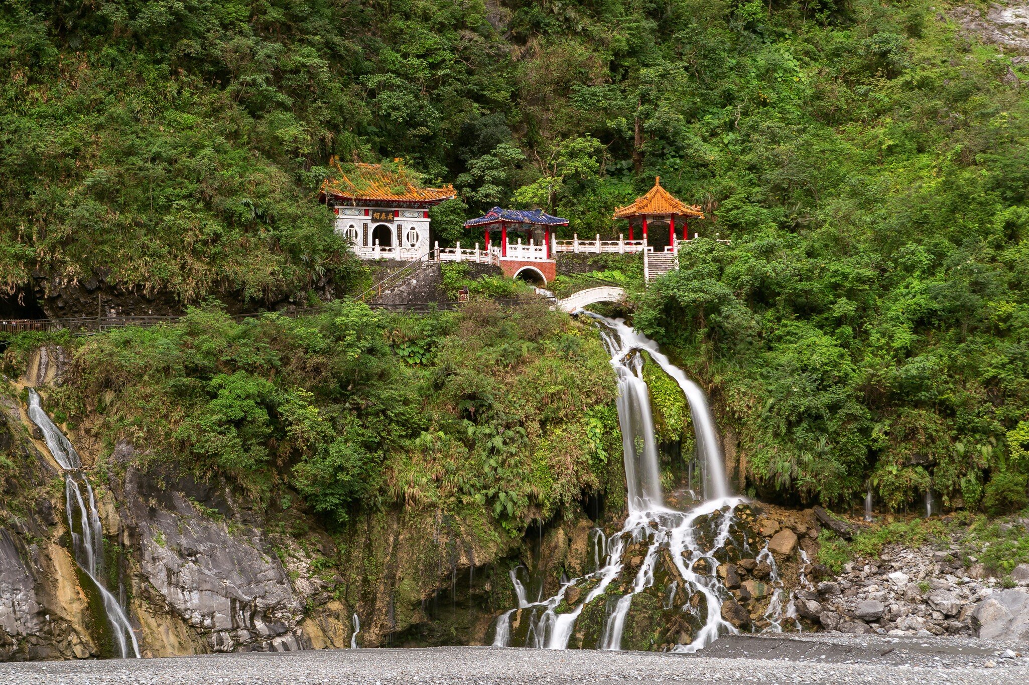 Eternal Spring Shrine surrounded by green trees and waterfall flowing over rocks below at Taroko National Park in Hualien, Taiwan.