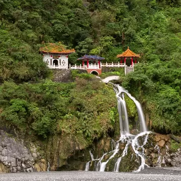 Eternal Spring Shrine surrounded by green trees and waterfall flowing over rocks below at Taroko National Park in Hualien, Taiwan.
