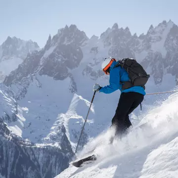 Skier making turn in powder snow with mountains in background.