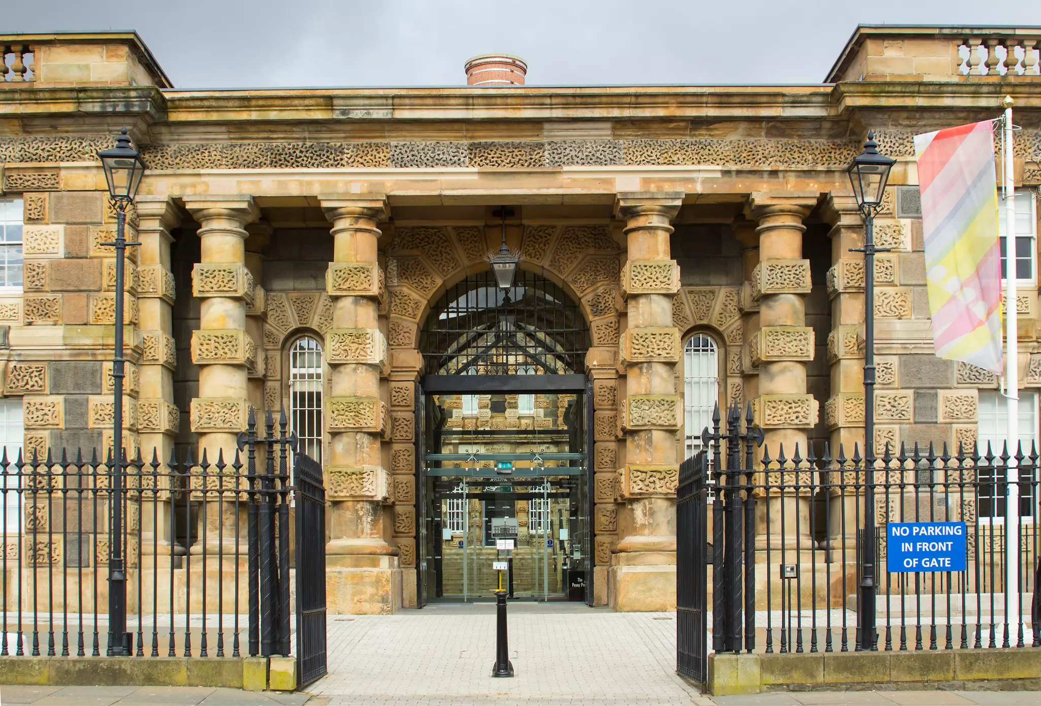 Black iron gates open to a tan stone building in Belfast.