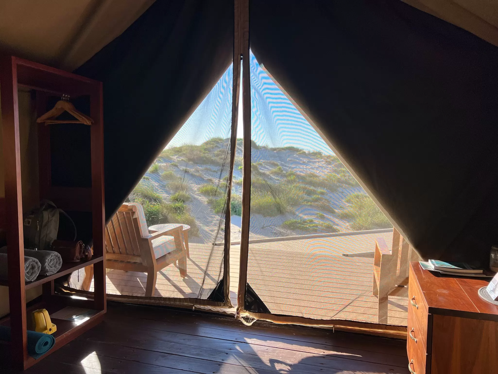 From inside a safari tent looking out to a view of sand dunes and sunshine.