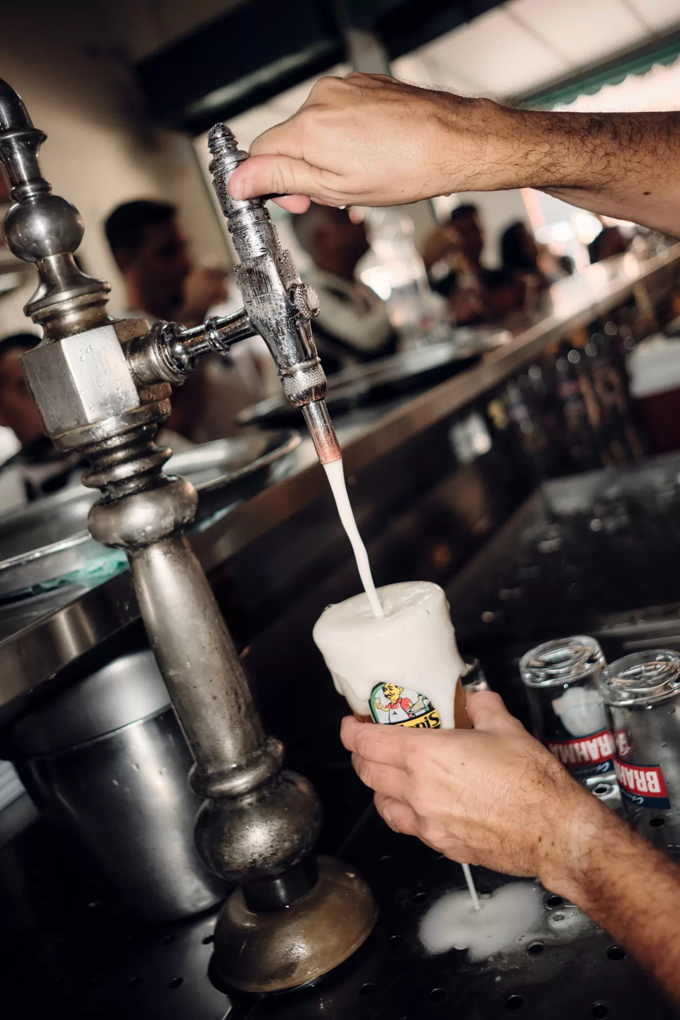 A man pouring beer from a silver tap; it's foamy, and the glass is overflowing.