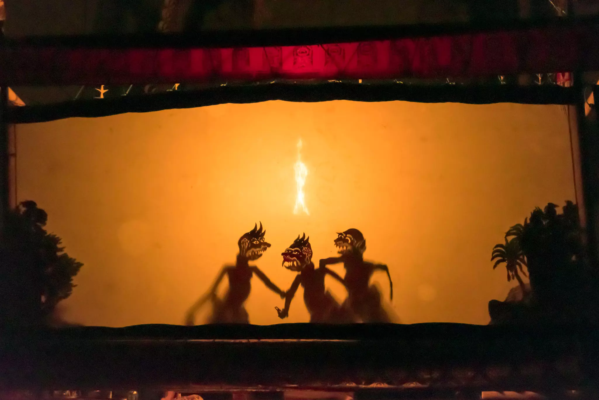 Three puppets are seen in silhouette against a curtain as part of a traditional performance.