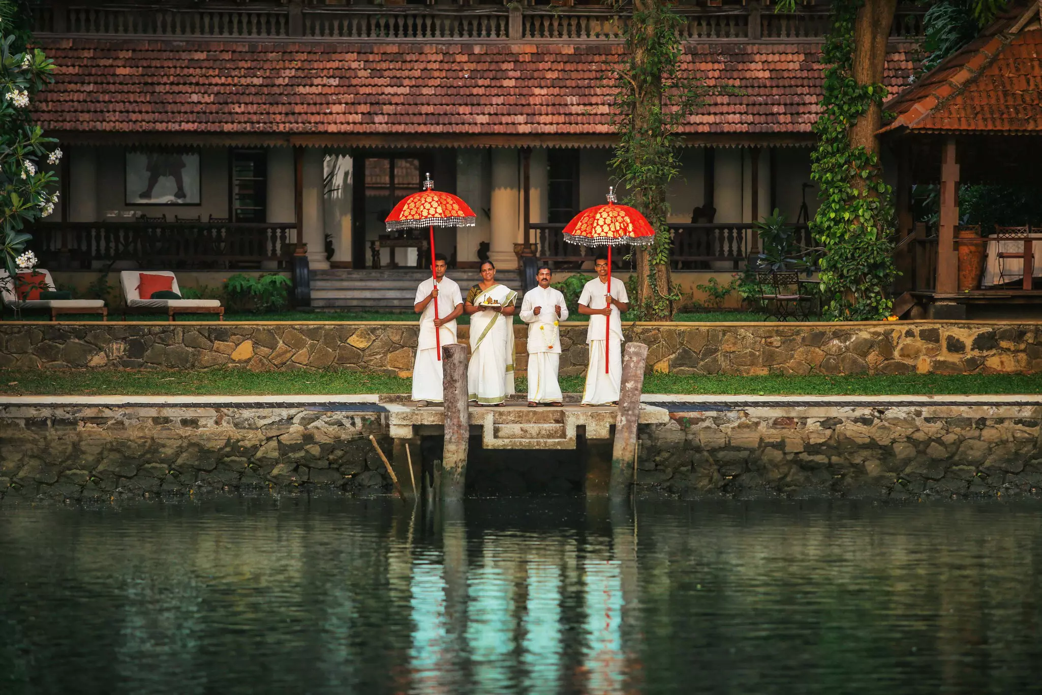 Four members of staff wait on a small hotel jetty to welcome guests approaching by boat