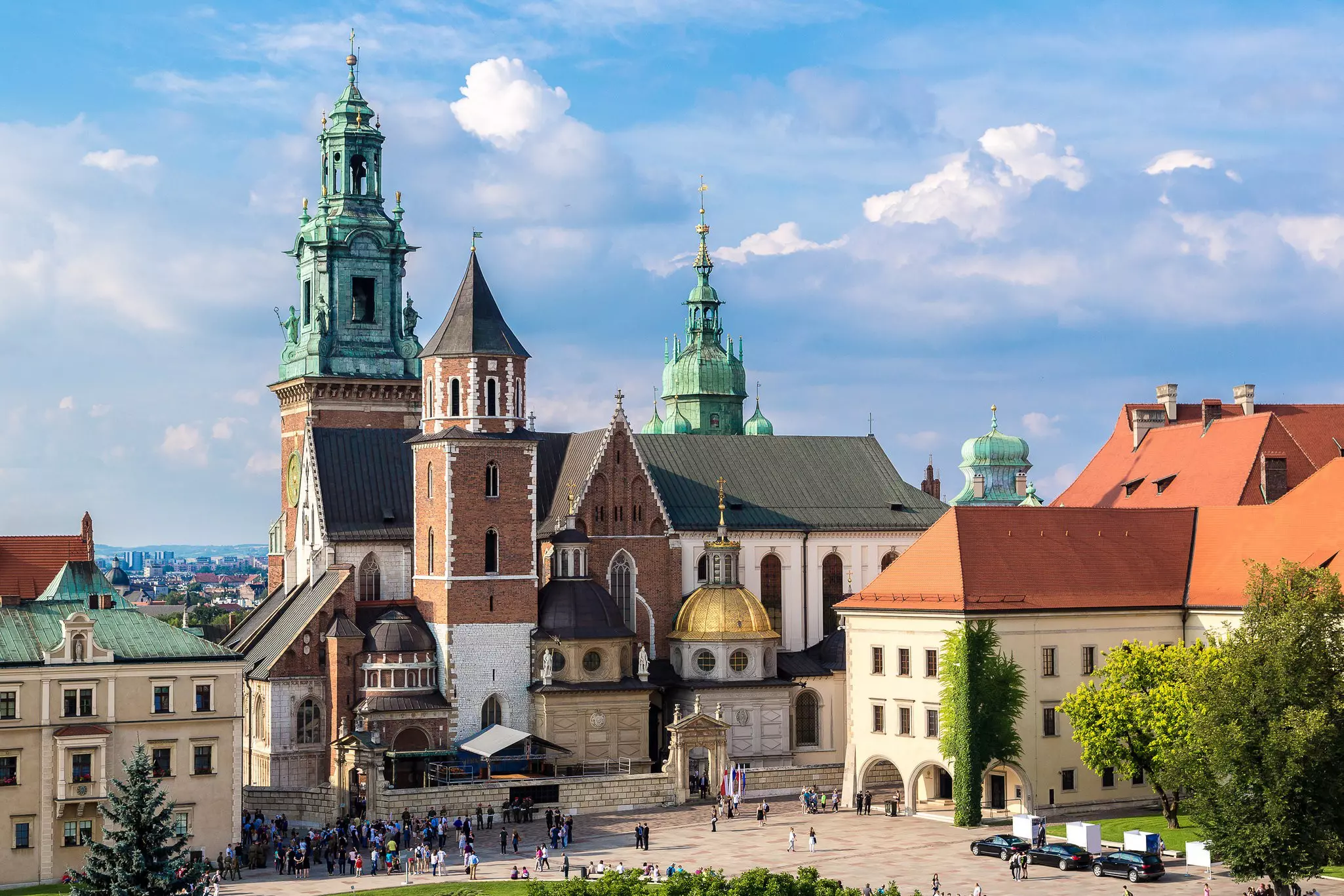 A church with a green bronze-clad spire, a brick tower and a low gold dome; people are in the courtyard in front.