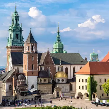 A church with a green bronze-clad spire, a brick tower and a low gold dome; people are in the courtyard in front.