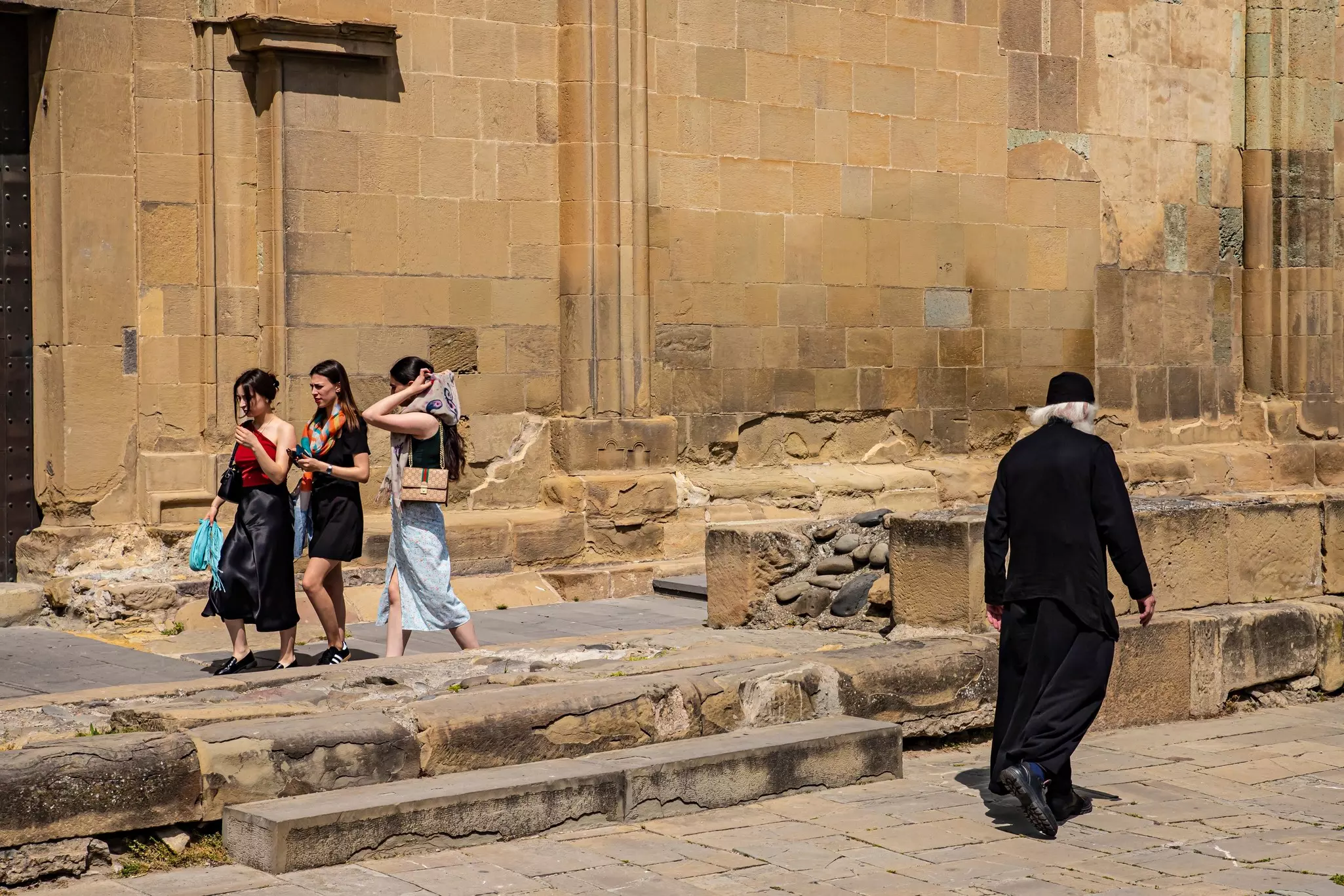 Three women walk by a yellow-stone cathedral