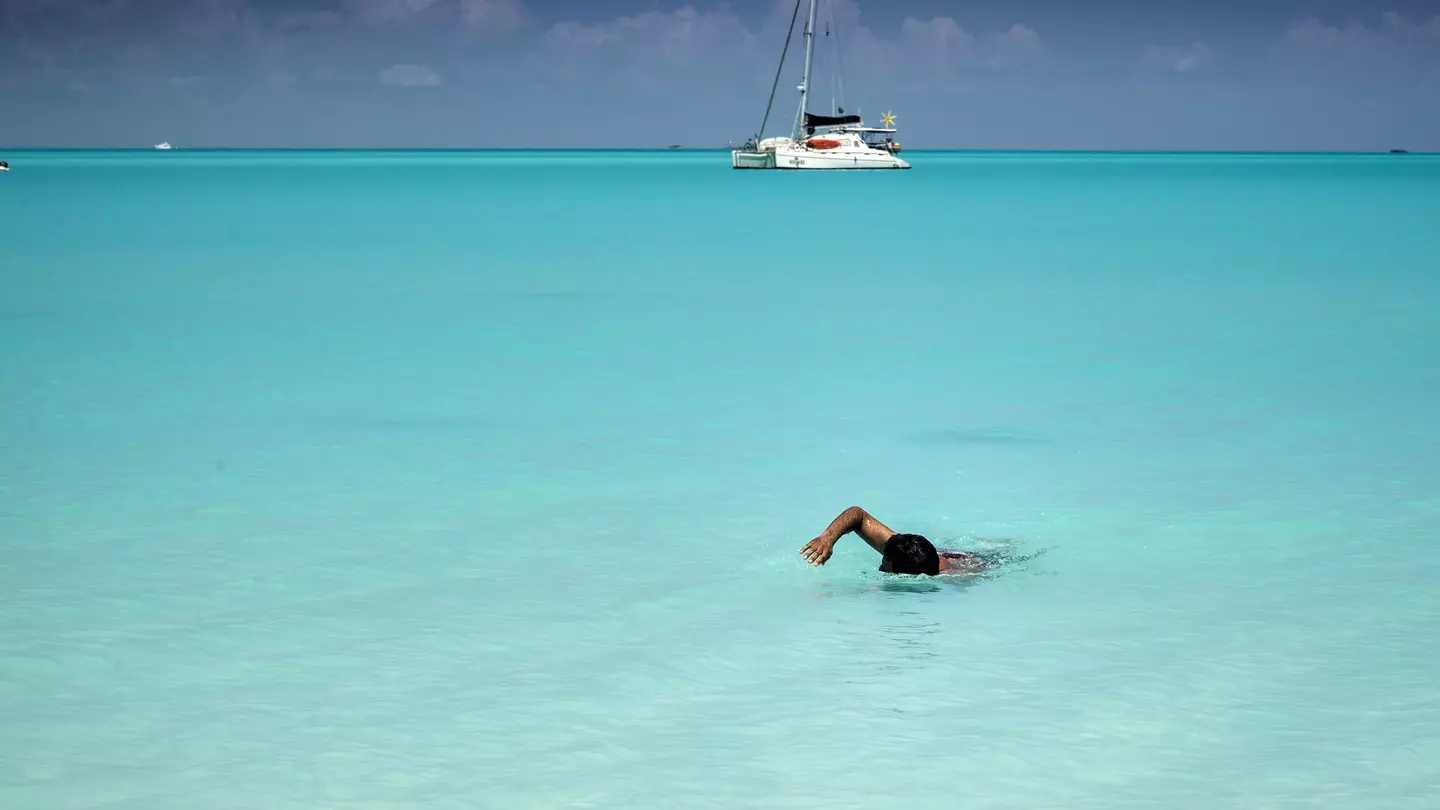 Man swimming to shore in perfectly clear turquoise-colored water.