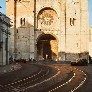 Lisbon Cathedral at sunset on a half-empty street with curvy tram tracks, in Lisbon, Portugal.
