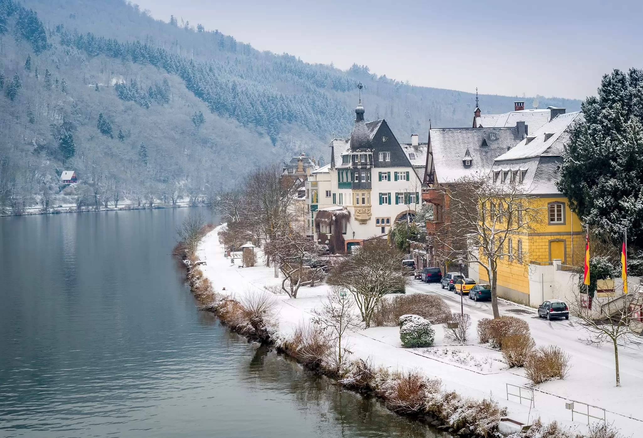 A bend in the river in Traben-Trarbach village covered in snow with fir trees on a hill across the way