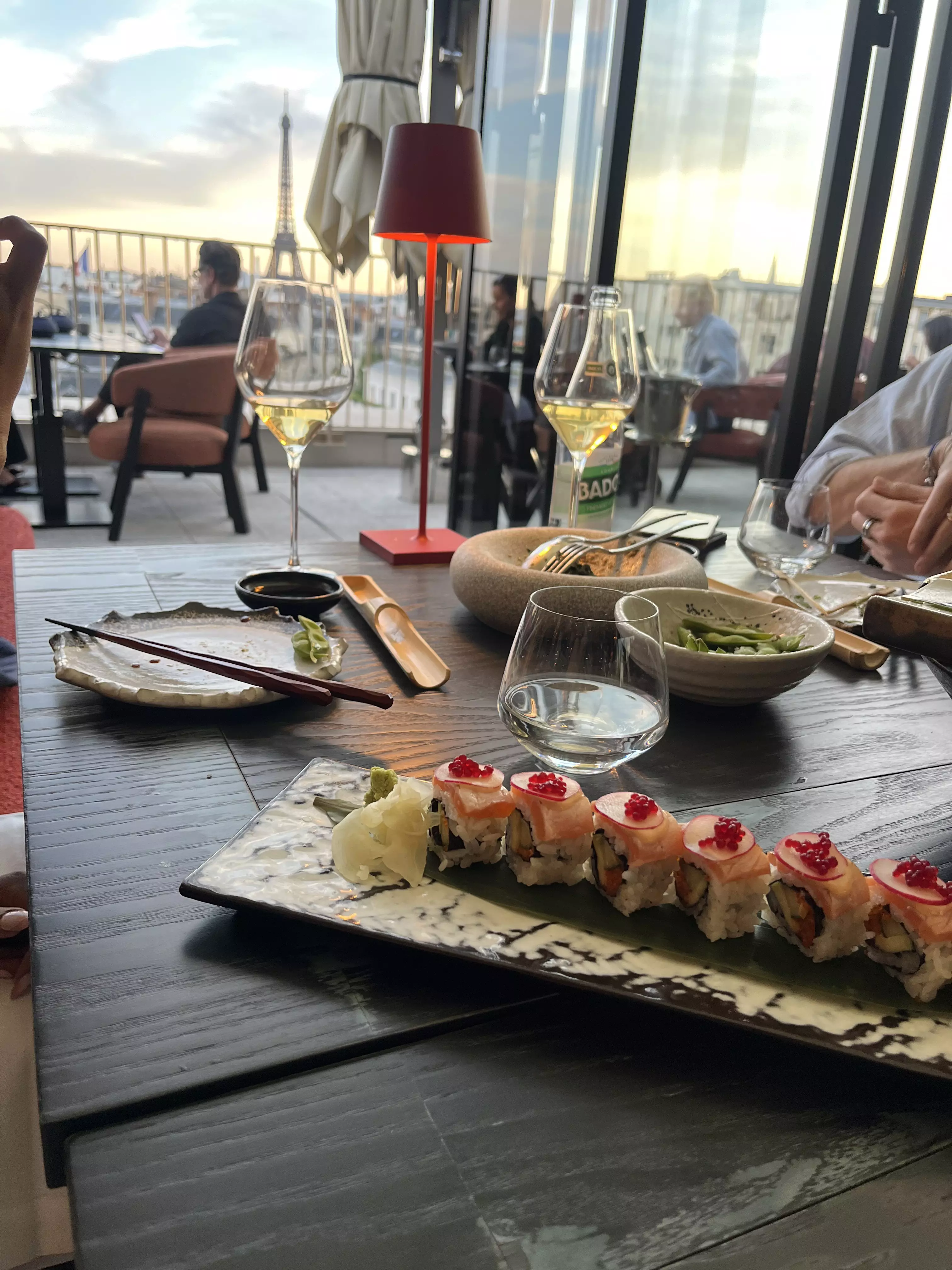 A neatly presented tray of sushi and two glasses of wine in a restaurant. Through the windows, a large iron tower dominates the skyline