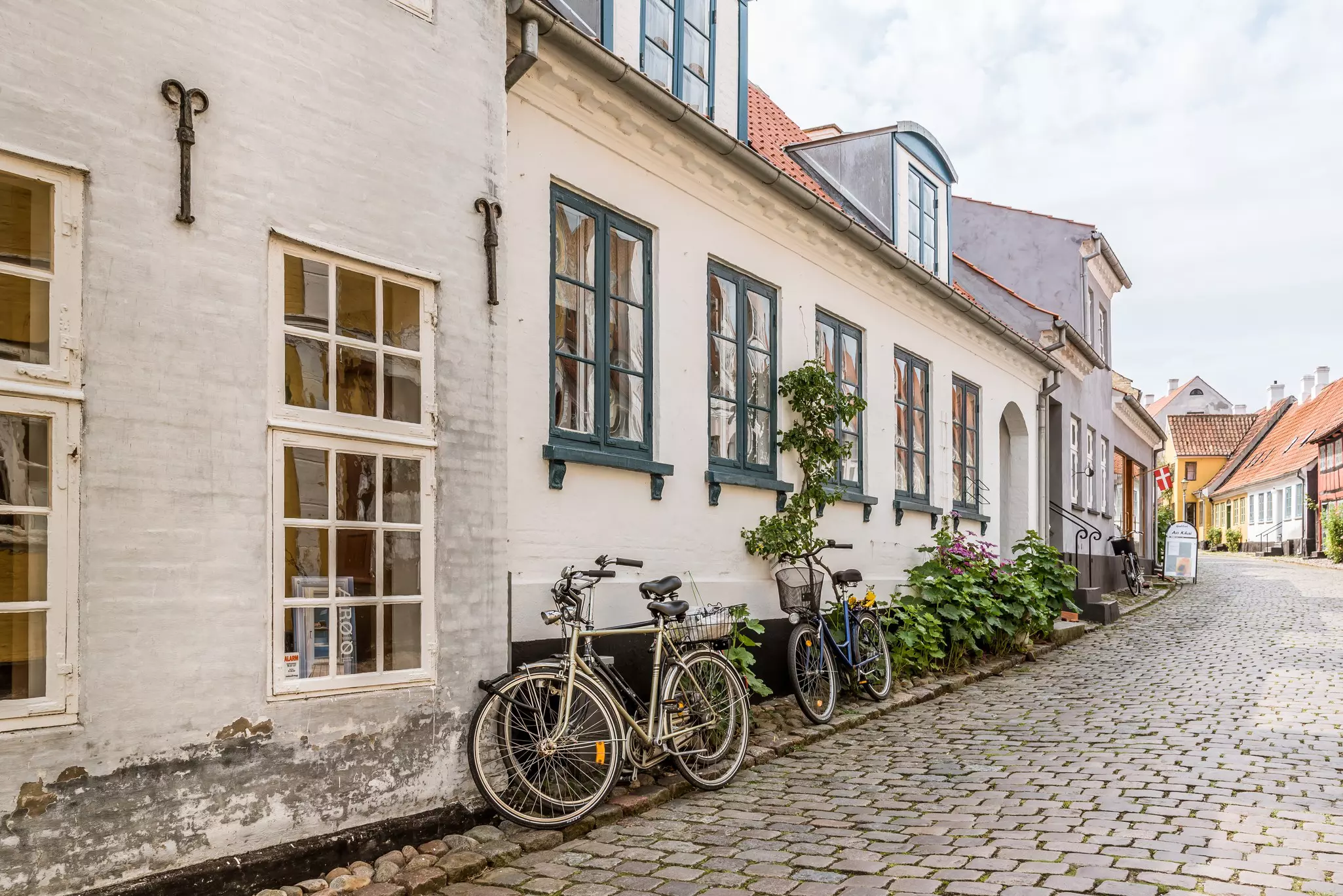 Bicycles lean against the walls of white-painted houses along a cobbled street in a village.