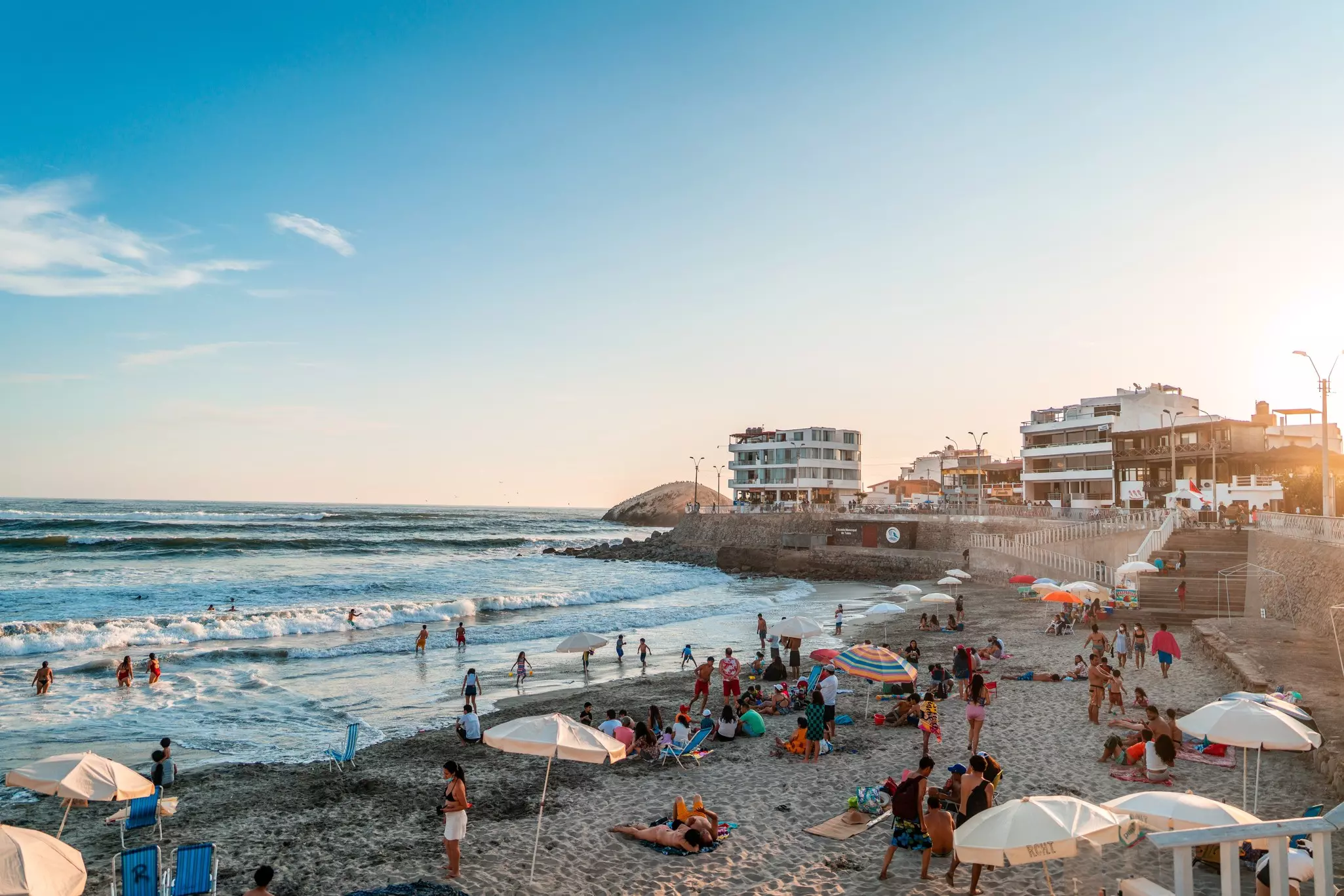 people and umbrellas on a beach with waves of water