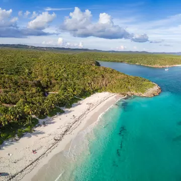 Aerial view of a sandy coastline with the ocean to the right and forest to the left and in the distance on a sunny day.