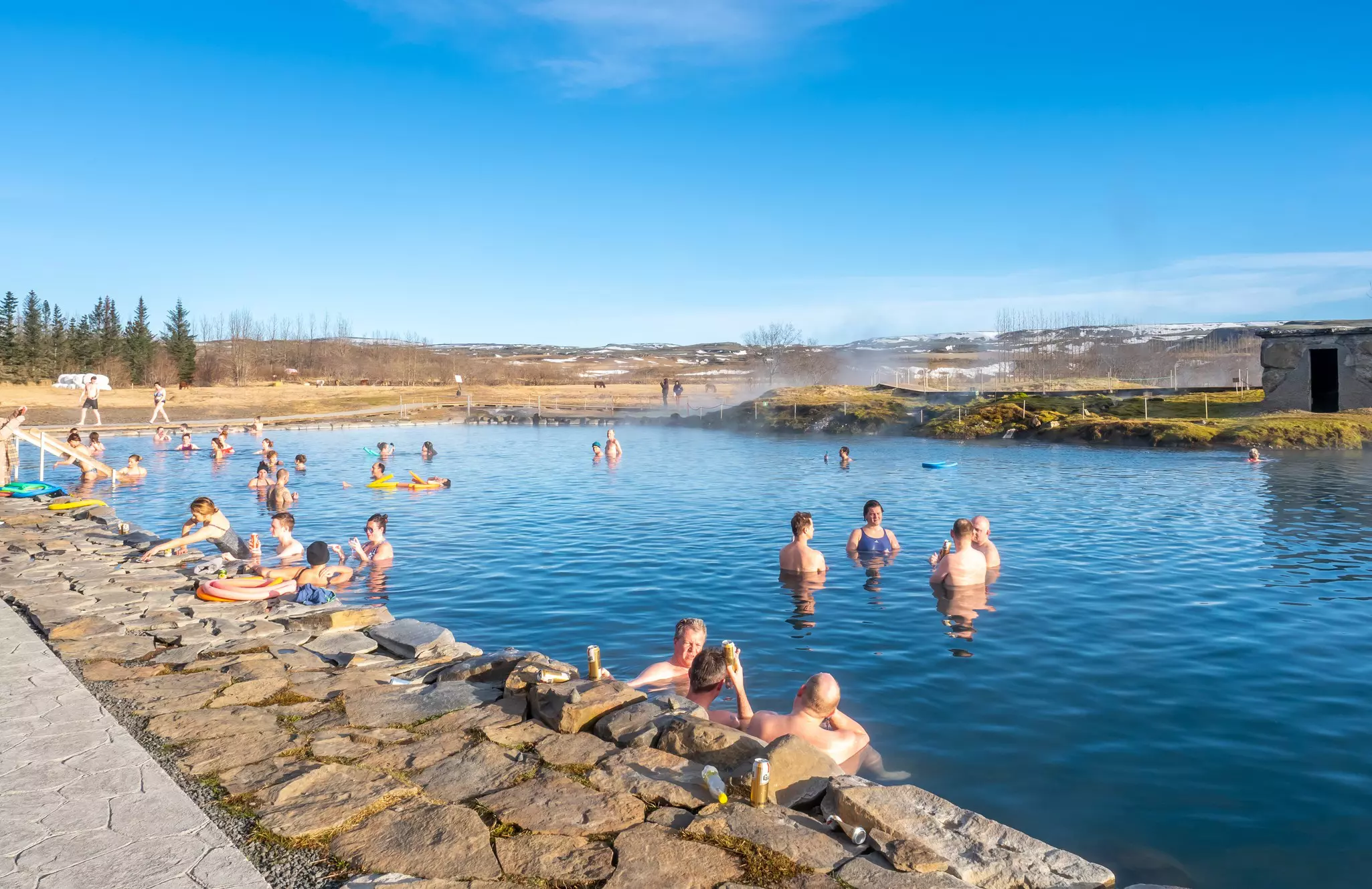 People relaxing in Secret lagoon hot spring, public outdoor warming swimming pool, landmark of small city of Flúðir, Iceland. 