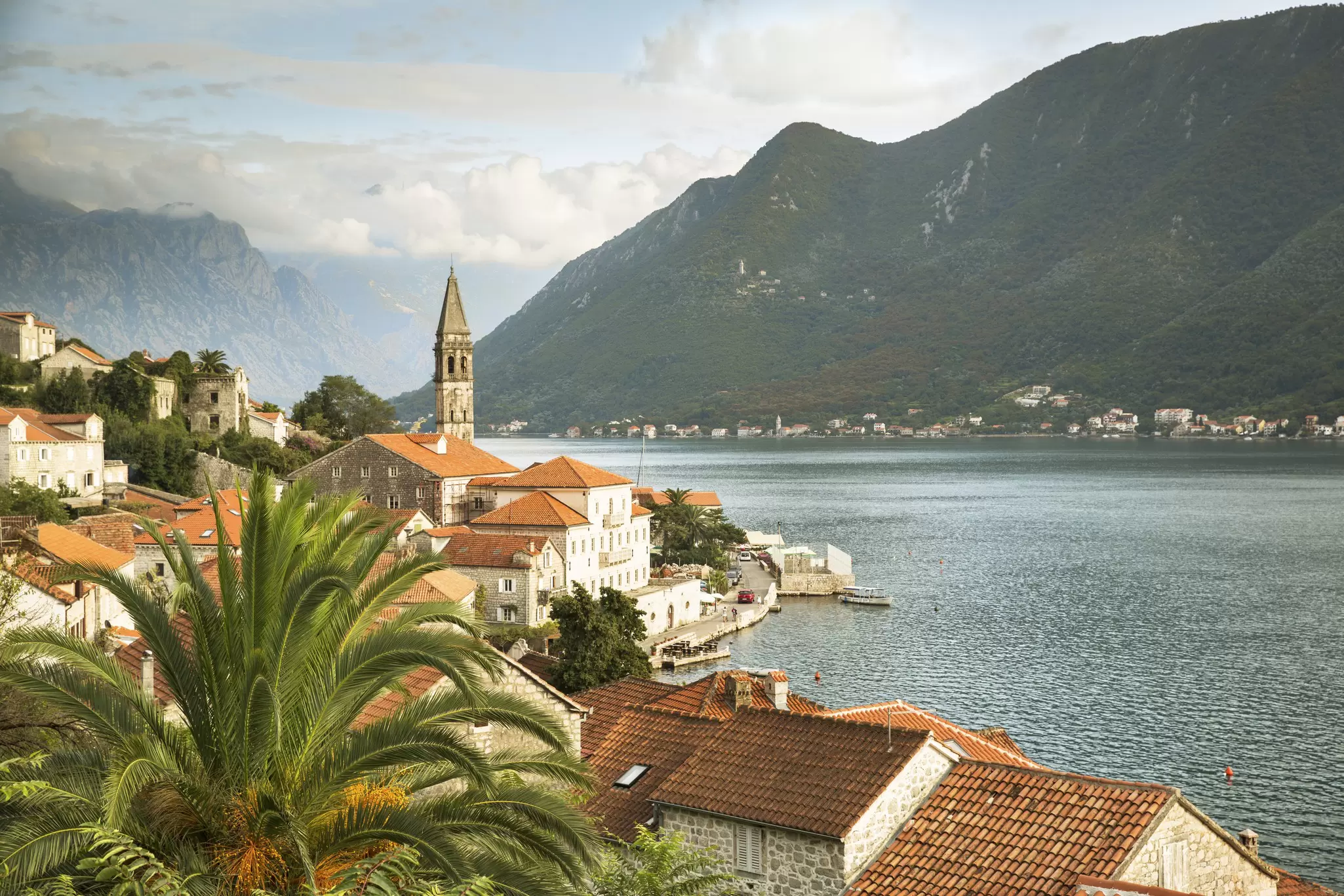A church spire stands tall above a small waterfront village on the Bay of Kotor, Montenegro