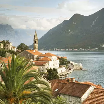 A church spire stands tall above a small waterfront village on the Bay of Kotor, Montenegro