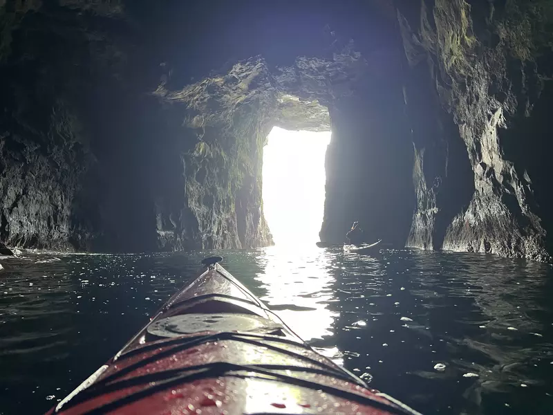 Front of a red kayak in a green/blue ocean looking out of a cave entrance