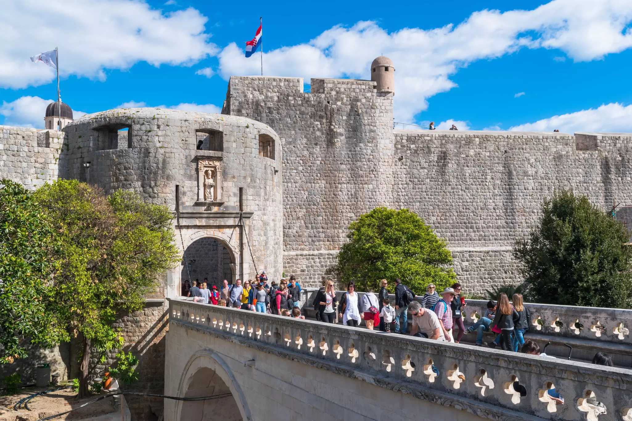 A line of people entering a walled city through a fortified stone gate tower