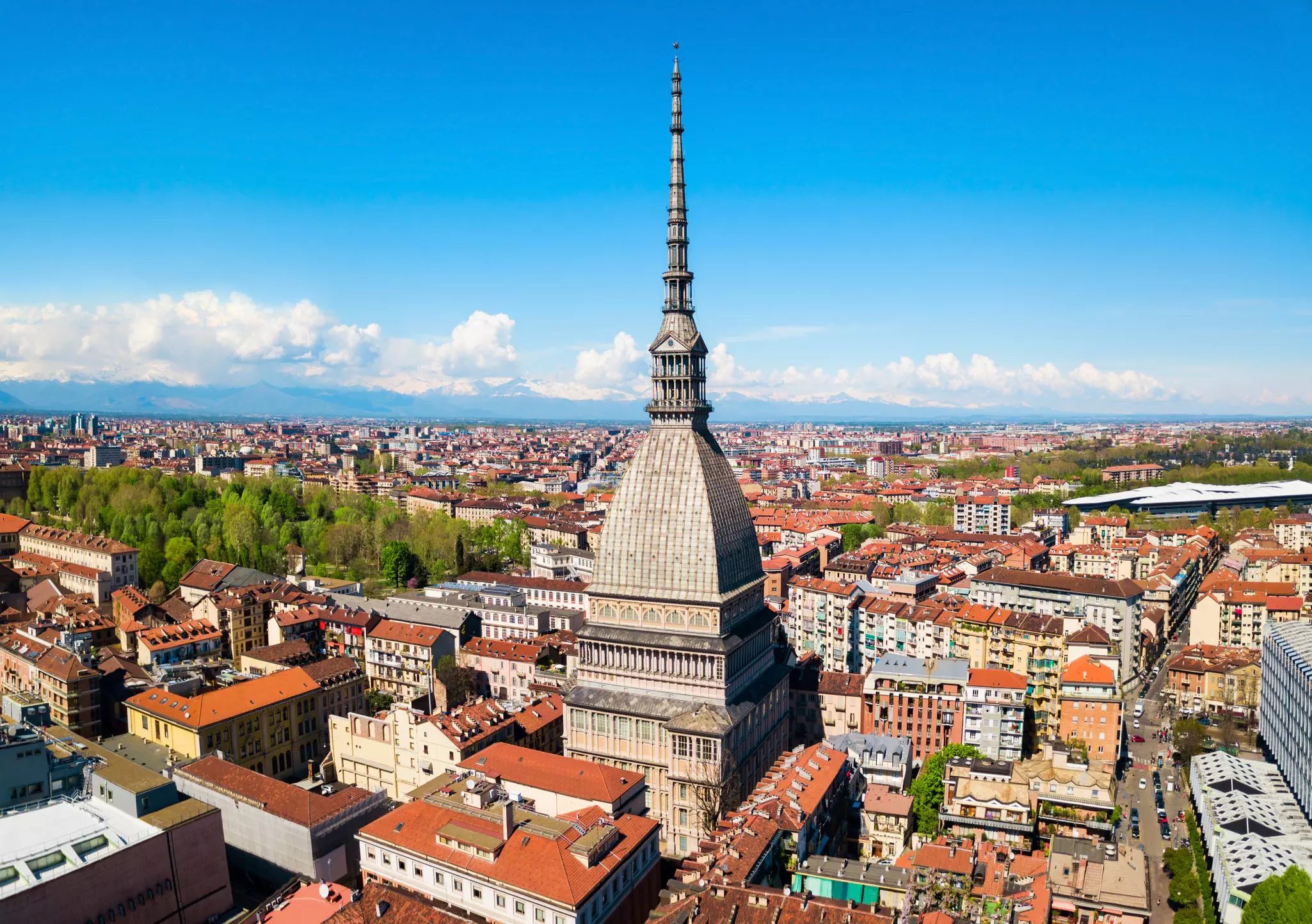 An aerial view of an unusually shaped tower surrounding lower red-roofed buildings in a city.