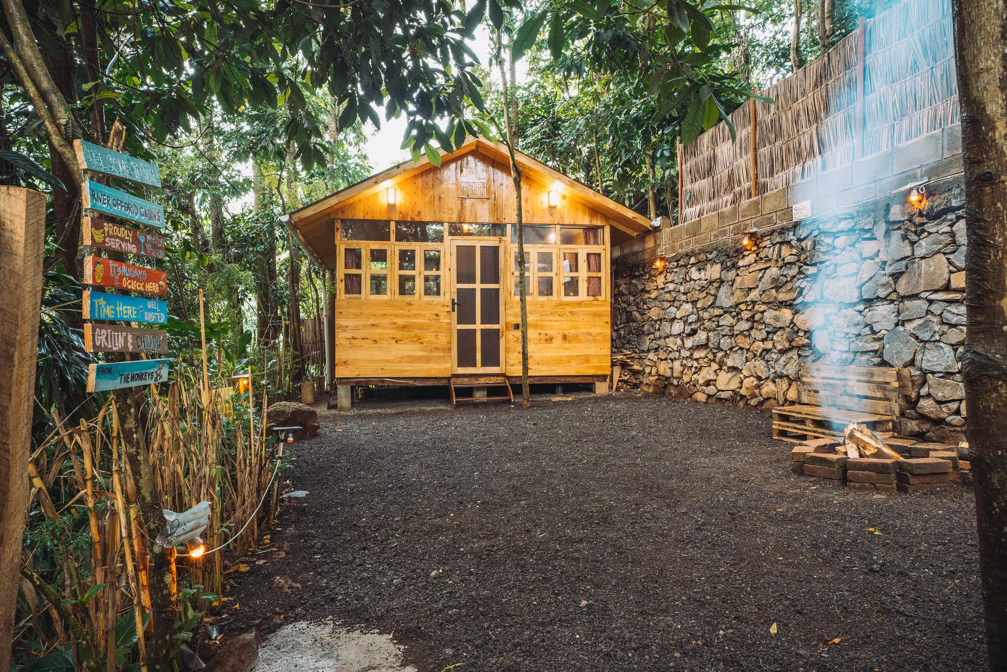 A fire burns in a pit near a wooden cabin at a hostel.