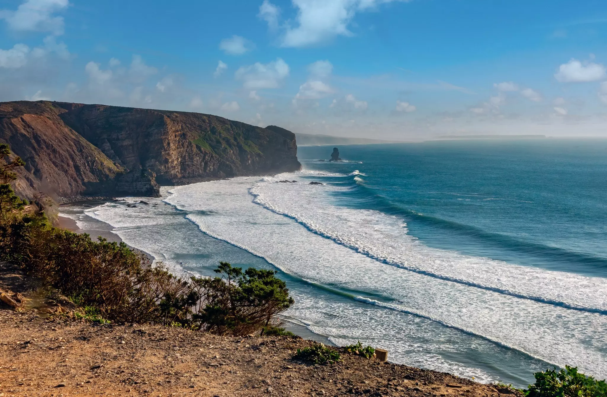 A view of a beach with whitecapped waves coming ashore and cliffs in the distance.