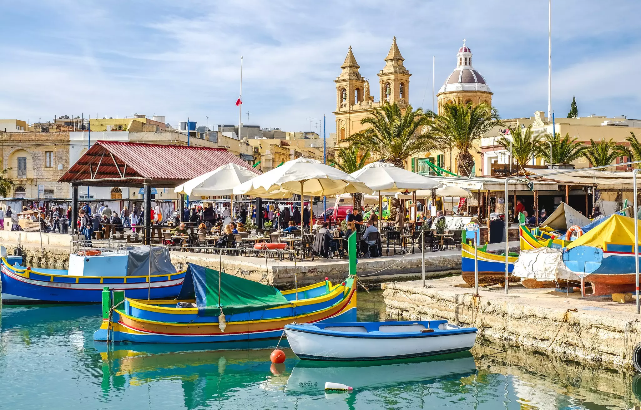 Colorful boats and charming buildings in the old fisherman village of Marsaxlokk, with people enjoying outdoor dining