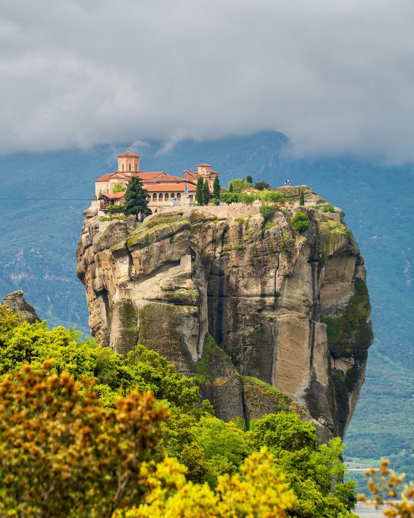 Holy Trinity Monastery perched on a sheer sandstone pillar at Meteora, Greece, under low cloud with green trees below