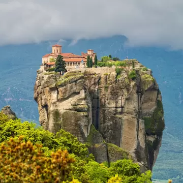Holy Trinity Monastery perched on a sheer sandstone pillar at Meteora, Greece, under low cloud with green trees below