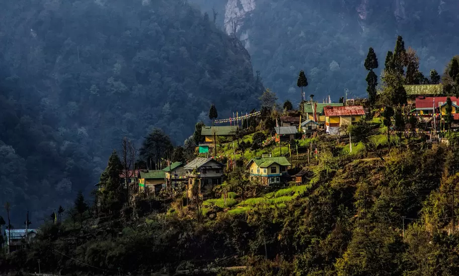 Hillside village of colourful tin-roofed houses with prayer flags on a forested ridge below misty mountains in Sikkim, India