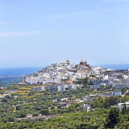 A town with white buildings covers a hilltop in Italy by the sea.