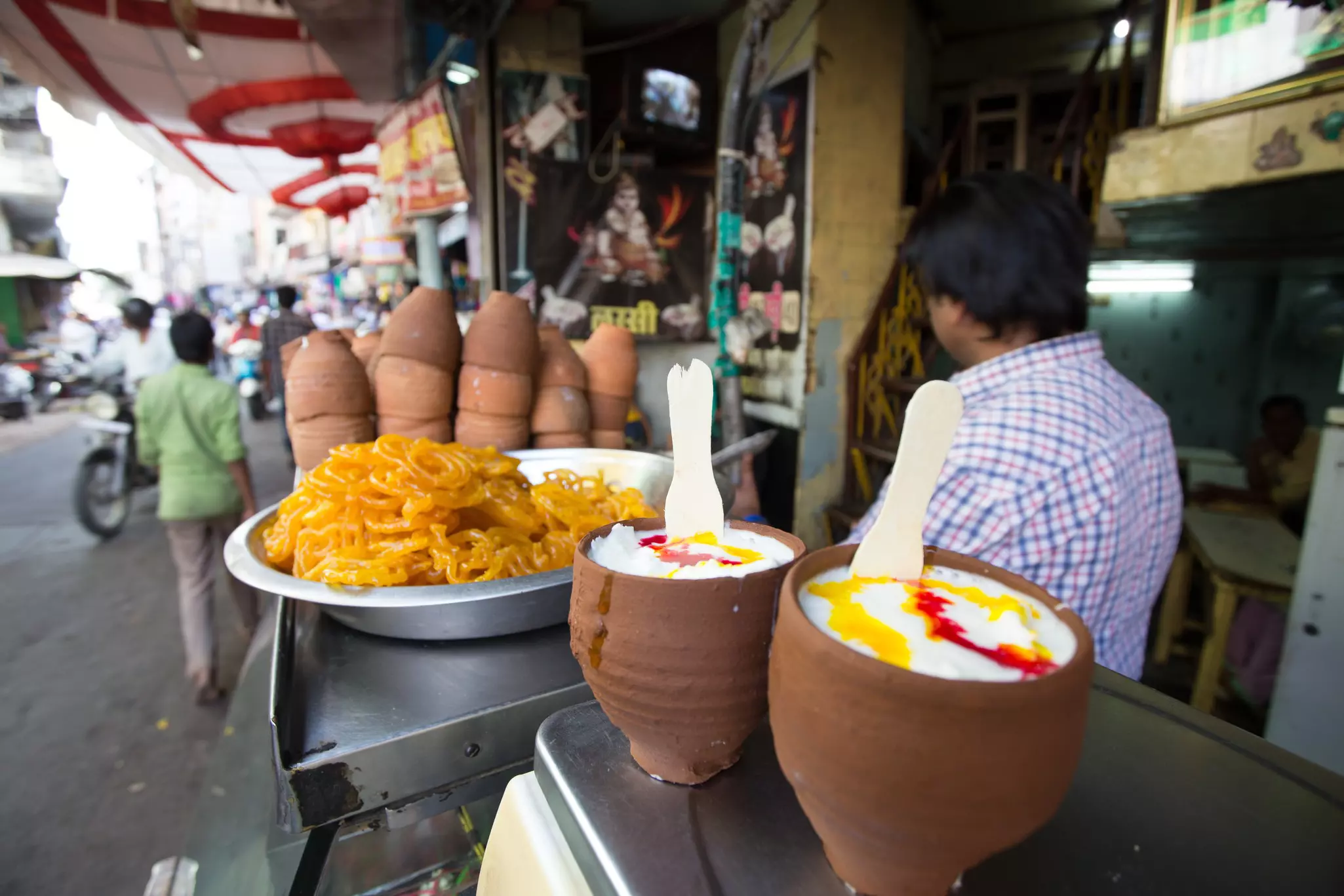 Yogurt drinks in clay pots sit atop a counter at a stall in a market on a busy city street.
