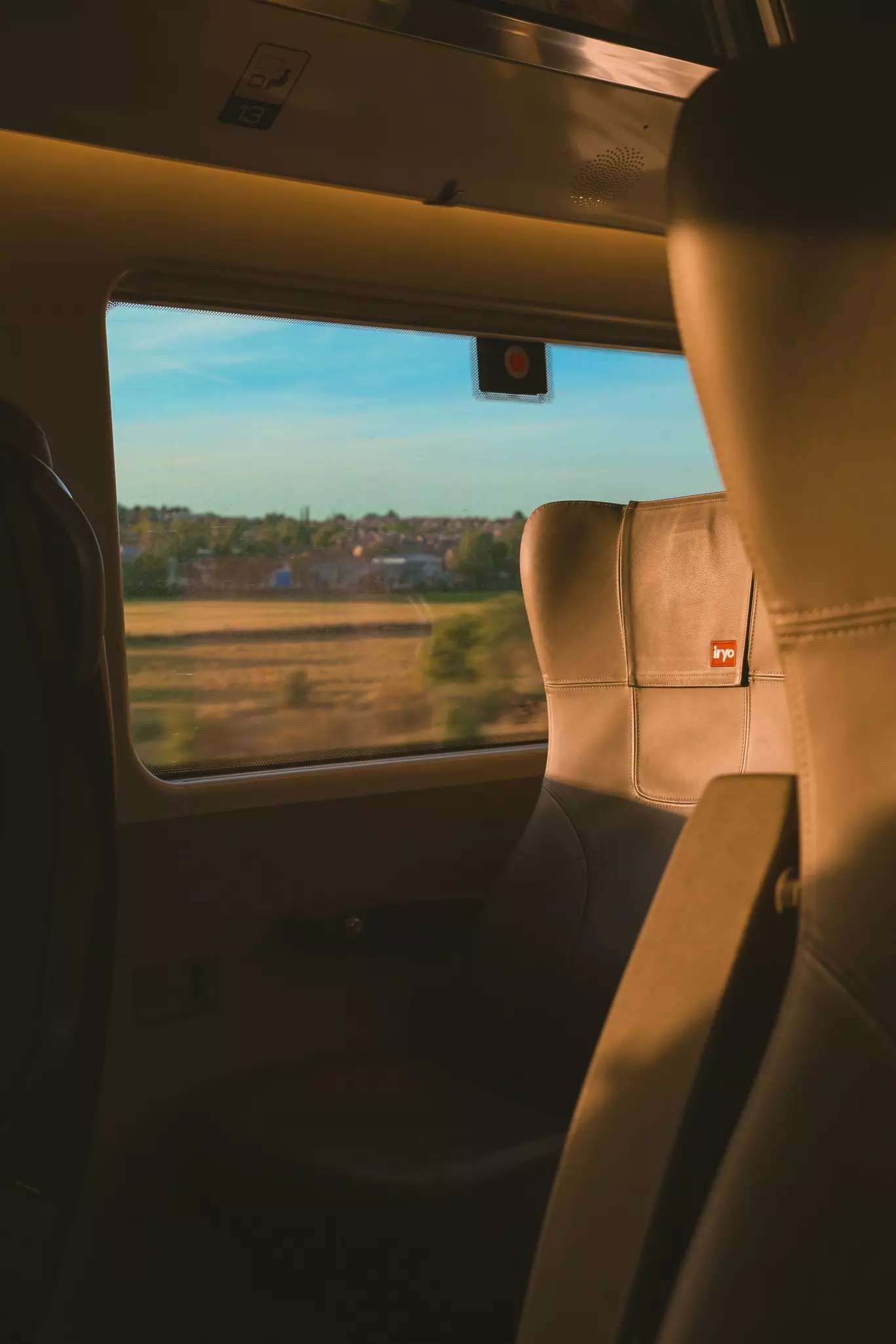 An empty window seat on a train passing fields bathed in sunlight at high speed.