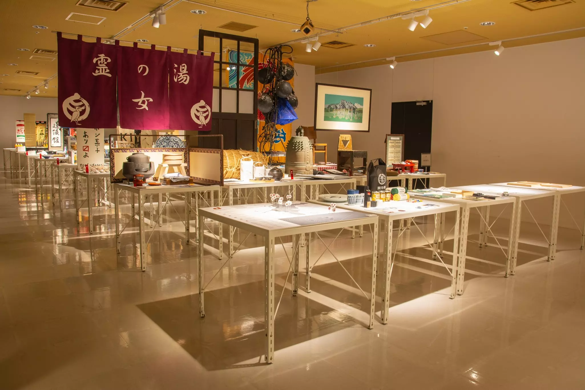 A gallery space contains a set of tables that display artworks in various media.