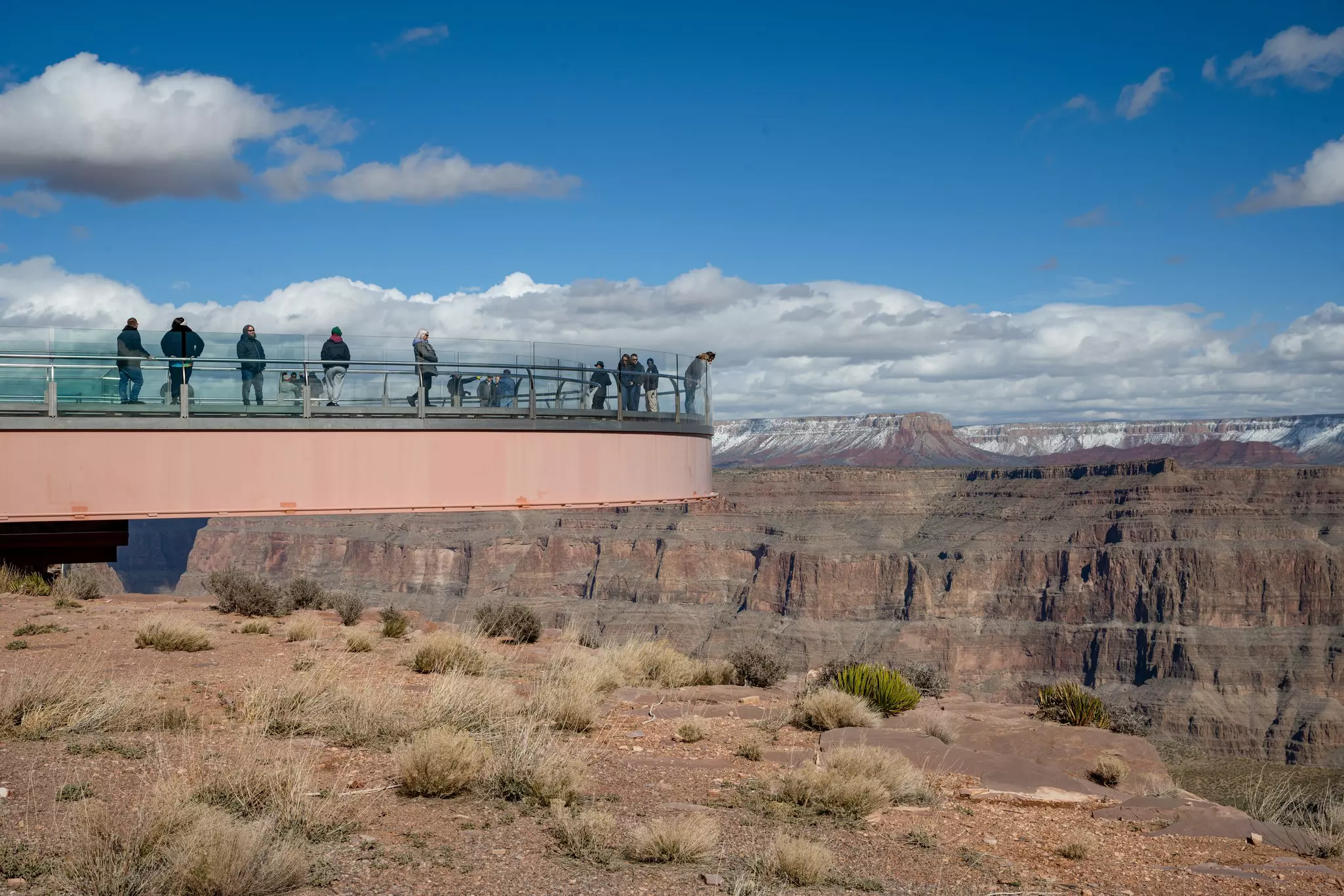 People on a walkway that juts out high above a vast canyon.