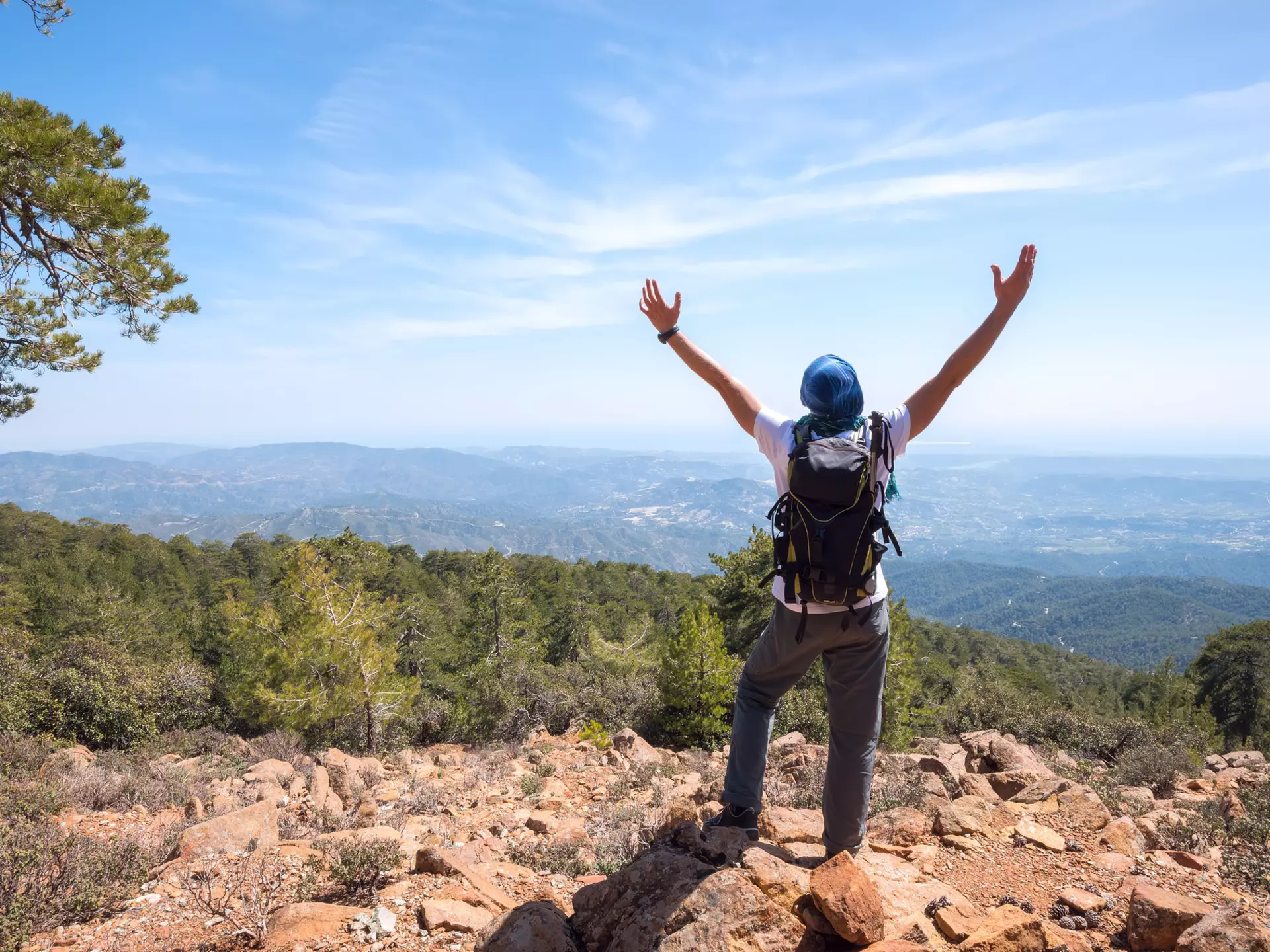 Happy man with backpack stands on a rocky slope, stretching his arms to the sky, crowded impressions of the travel - sunny spring day in the mountains. National park Troodos, Cyprus. Back view.  License Type: media  Download Time: 2021-11-04T16:35:25.000Z  User: AMccarthy_lonelyplanet  Is Editorial: No  purchase_order:   