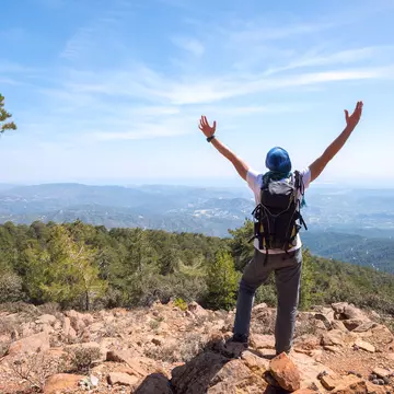 Happy man with backpack stands on a rocky slope, stretching his arms to the sky, crowded impressions of the travel - sunny spring day in the mountains. National park Troodos, Cyprus. Back view.  License Type: media  Download Time: 2021-11-04T16:35:25.000Z  User: AMccarthy_lonelyplanet  Is Editorial: No  purchase_order:   