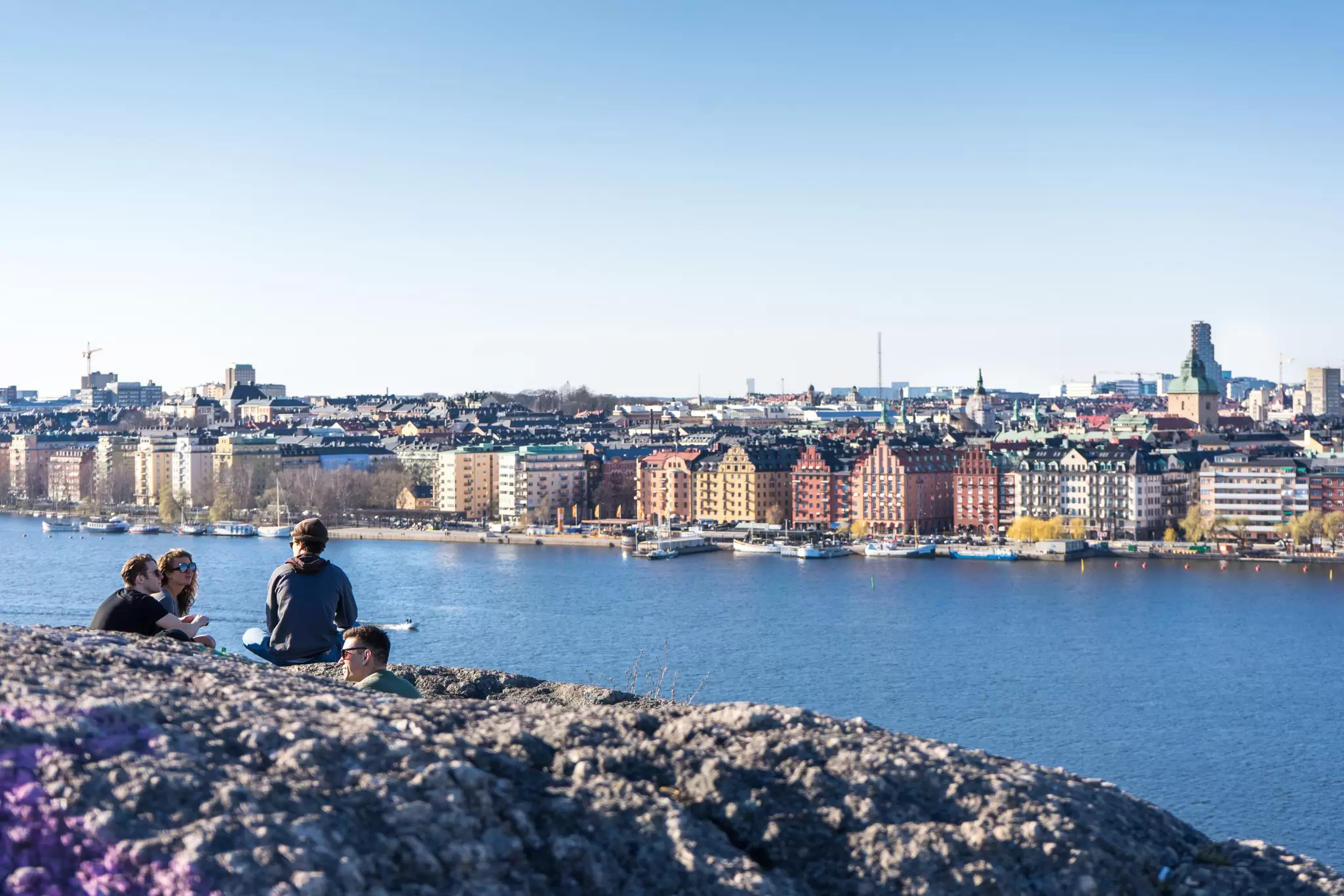 A group of people sit at a high point above a waterside city enjoying the view in the late evening sunshine; Stockholm, Sweden.