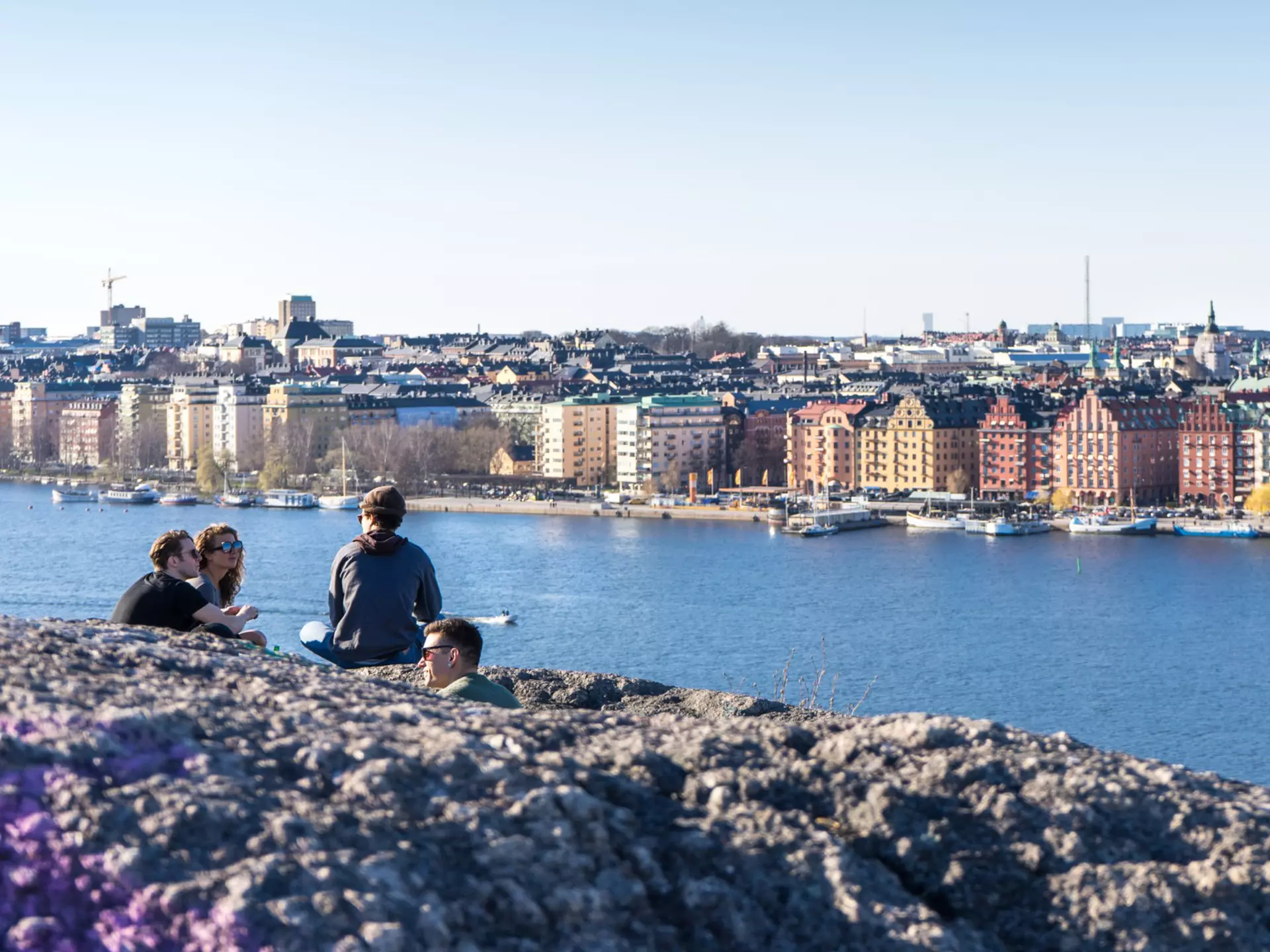 A group of people sit at a high point above a waterside city enjoying the view in the late evening sunshine; Stockholm, Sweden.